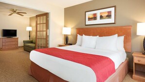 A hotel room with a large bed, a television, a desk with a lamp, and a ceiling fan. - Country Inn & Suites by Radisson, Davenport - Quad Cities (Davenport)