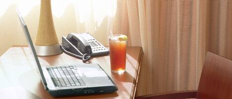 A wooden table with a laptop, a telephone, and a glass of iced tea.