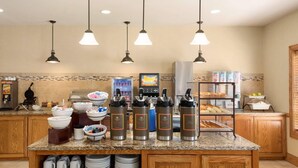 A breakfast bar with coffee makers, bowls, and a beverage dispenser. - Country Inn & Suites by Radisson, Davenport - Quad Cities (Davenport)