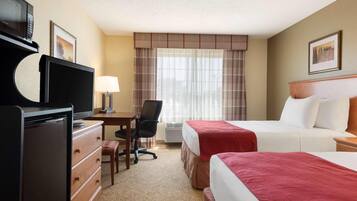 Quarto de hotel com cama, escrivaninha, cadeira, televisão e cômoda.