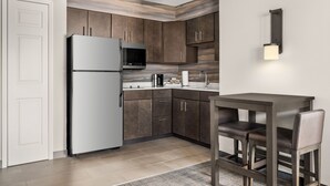 Una cocina moderna con armarios de madera oscura, un refrigerador de acero inoxidable, un microondas y un pequeño comedor con dos sillas.