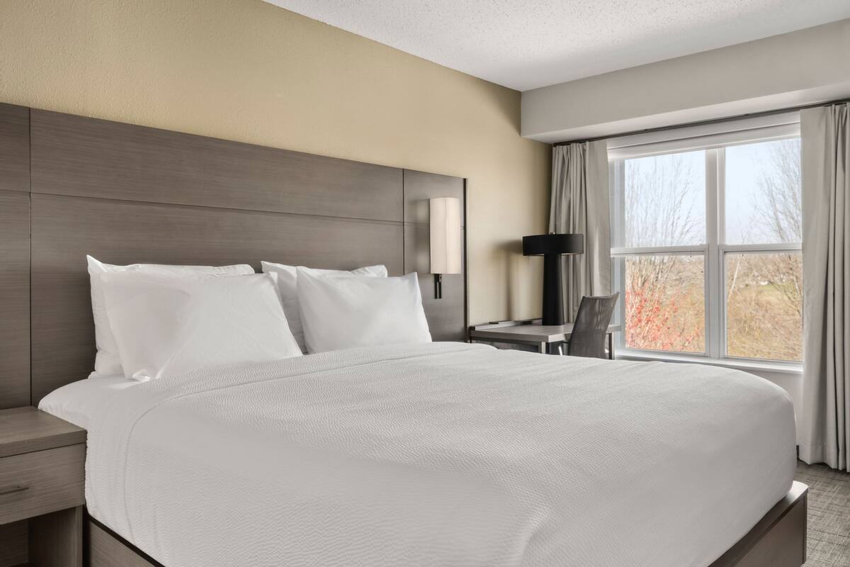 Una camera d'albergo con un letto grande, una scrivania, una sedia e una finestra con tende.