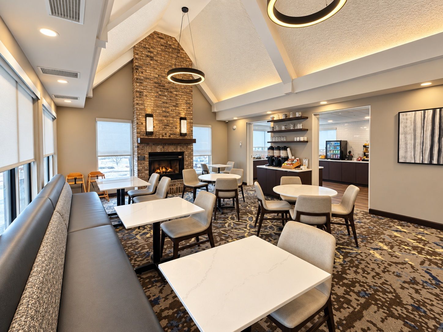 A hotel lobby with a fireplace, seating areas, and a kitchen in the background.