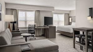 Habitación de hotel con sofá, escritorio y silla, cama, televisor y mesa con sillas.