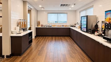 A modern kitchen with a wooden floor, white tiled walls, and a window providing natural light.