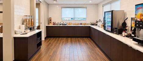 A modern kitchen with a wooden floor, white tiled walls, and a window providing natural light.