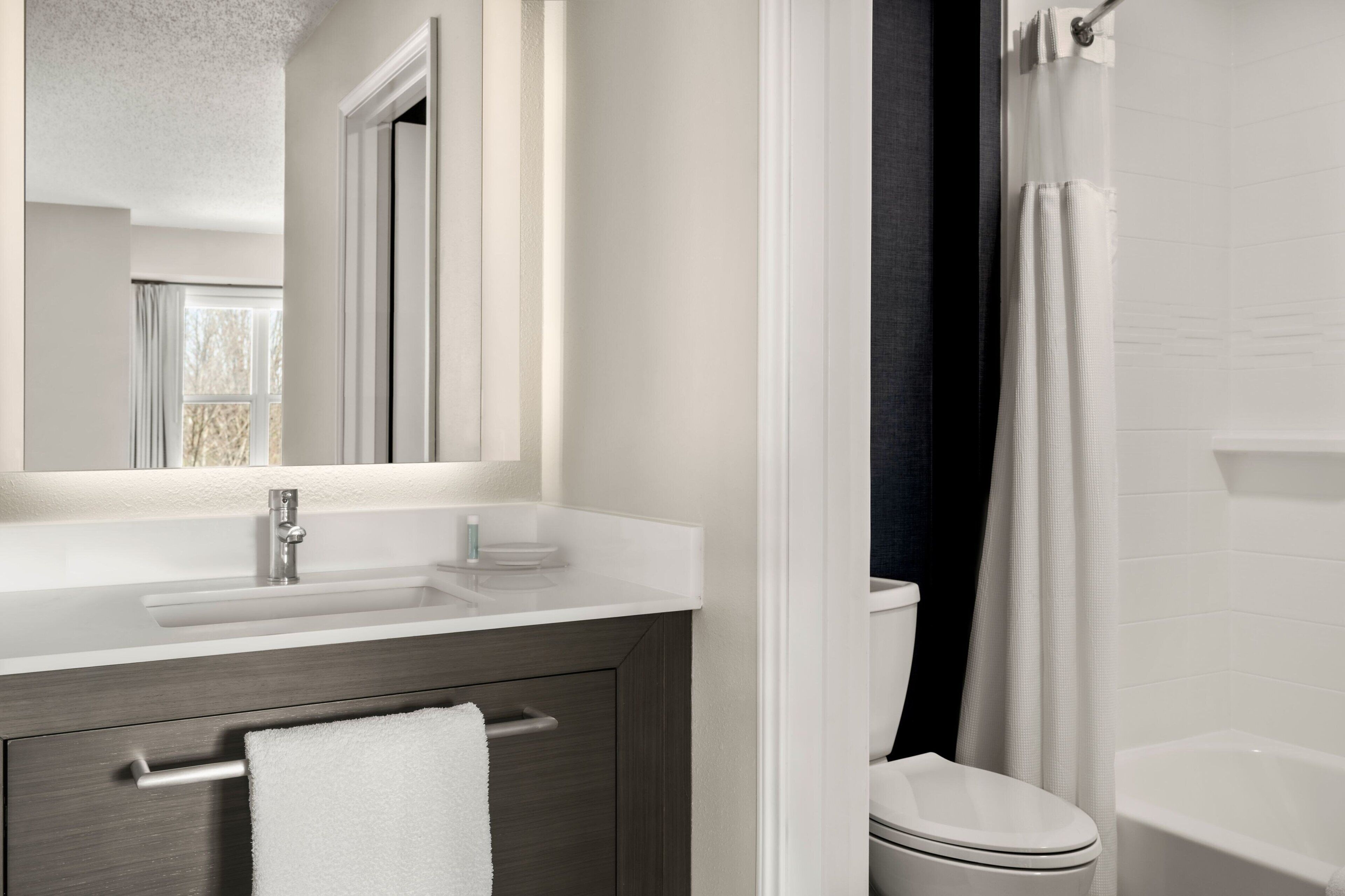 A modern bathroom with a white sink, dark wood vanity, a white toilet, and a shower with a white curtain.