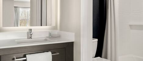 A modern bathroom with a white sink, dark wood vanity, a white toilet, and a shower with a white curtain.