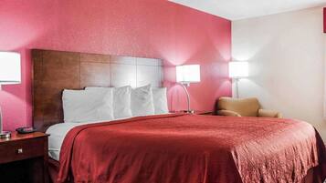Une chambre d’hôtel avec un grand lit, deux lampes de chevet, une tête de lit en bois et un mur d’accent rouge.