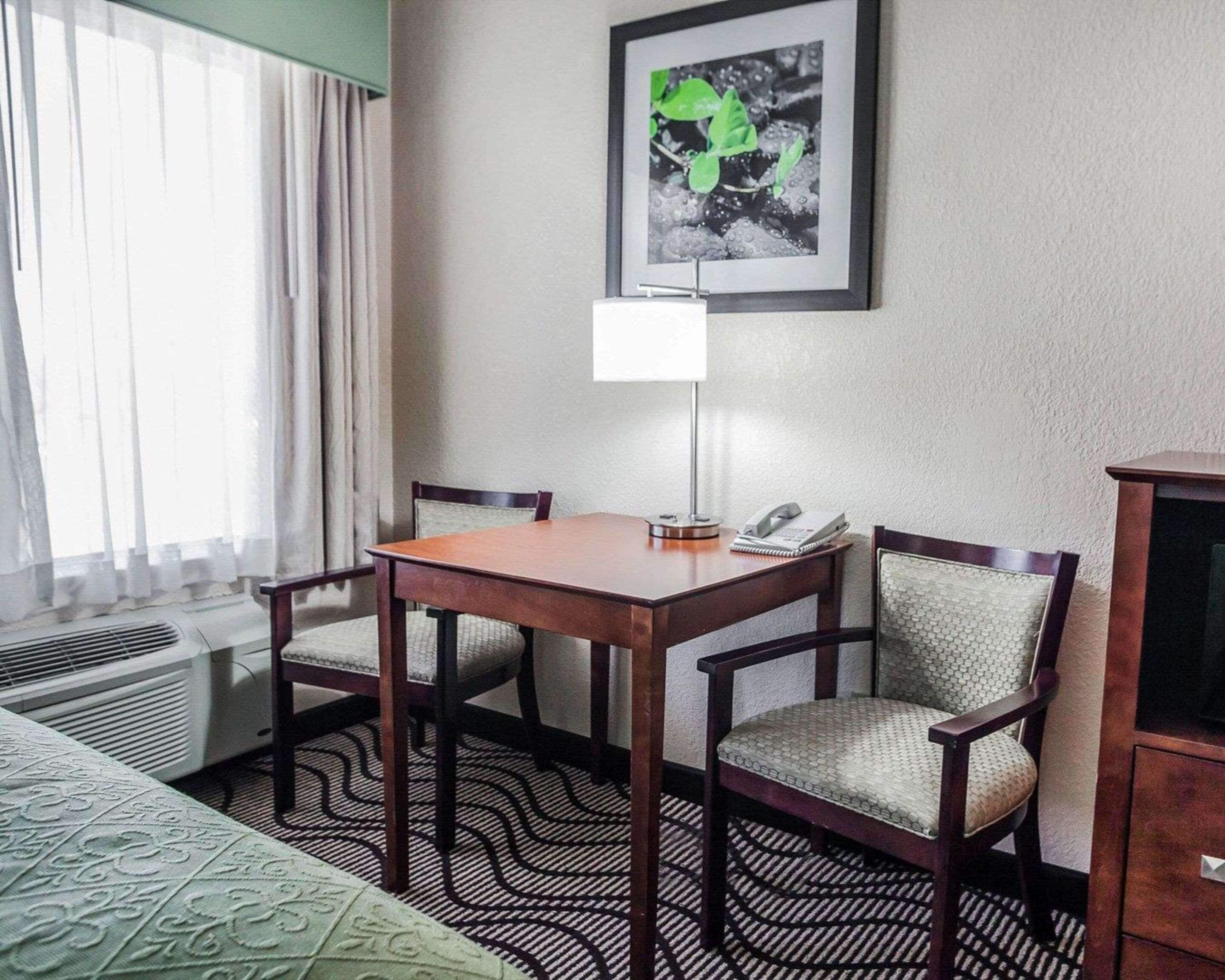 A hotel room with a wooden table, two chairs, a desk lamp, a telephone, and a framed picture on the wall.