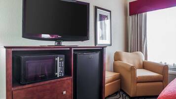 Ein Hotelzimmer mit Flachbildfernseher, Minibar, Kühlschrank und einem bequemen Sessel am Fenster.