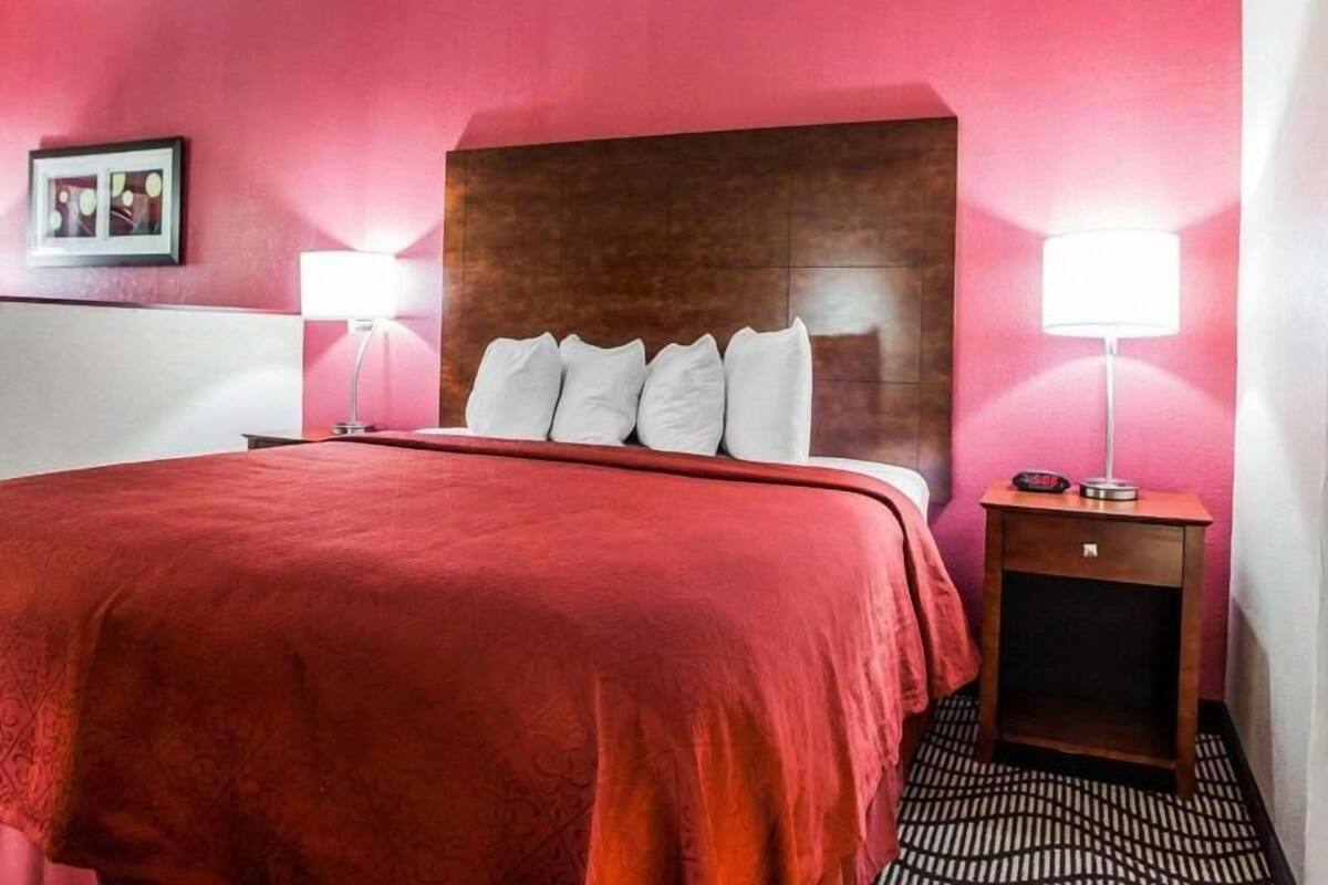 A hotel room with a large bed, two bedside lamps, a wooden headboard, a small bedside table, and a framed picture on the wall.