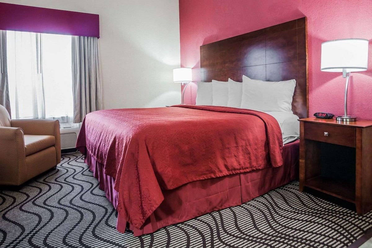 A hotel room with a large bed, two bedside lamps, a nightstand, and a chair.