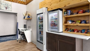 A kitchenette with a refrigerator, a microwave, and a shelf with snacks. - AmericInn by Wyndham Williamsburg (South Amana)