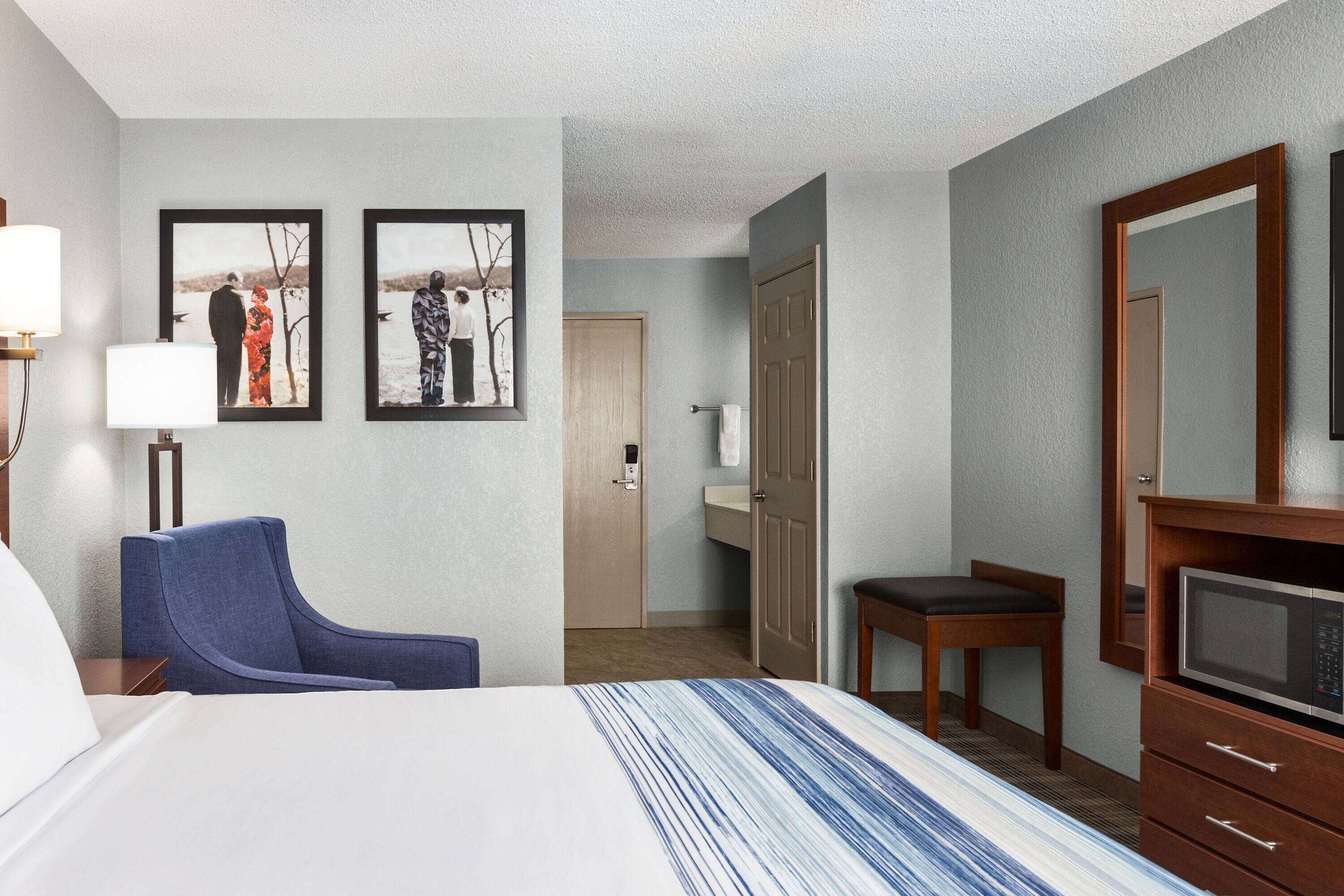 Ein Hotelzimmer mit einem Bett, einem Schreibtisch, einem Sessel, einem Fernseher und zwei gerahmten Bildern an der Wand.