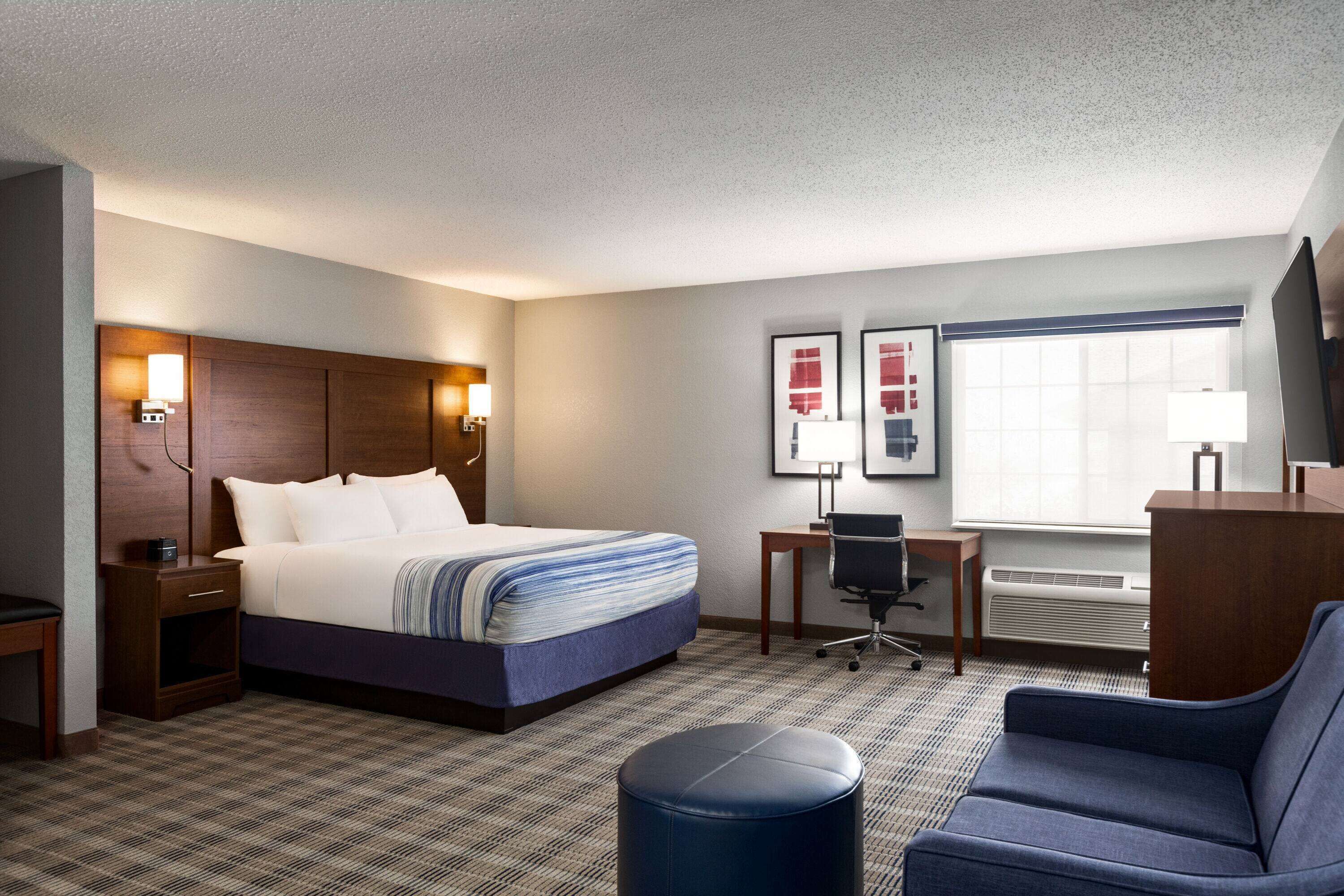 A hotel room with a bed, desk, chair, and a large window.