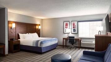 A hotel room with a bed, desk, chair, and a large window.