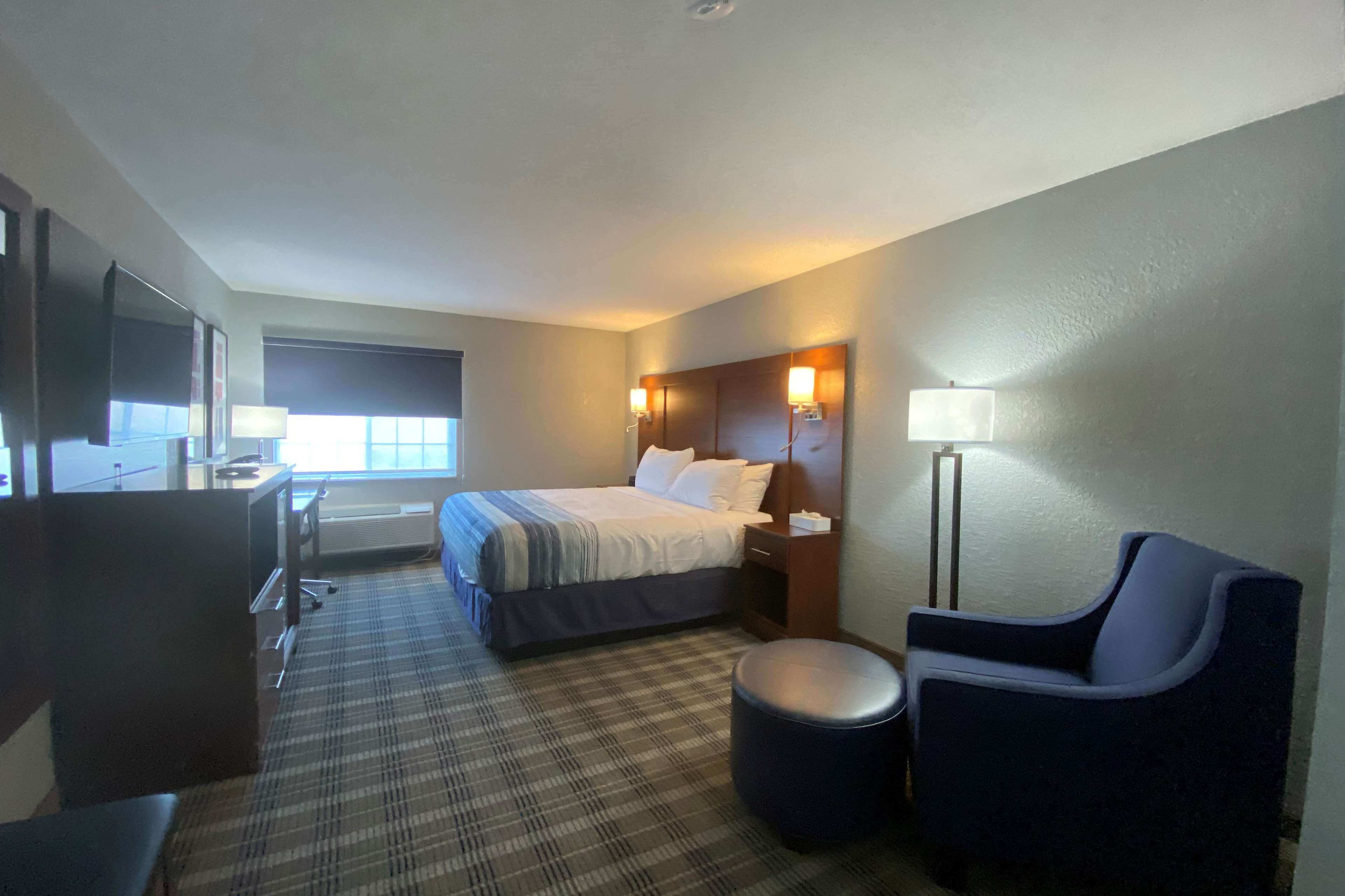 A hotel room with a bed, a desk, a chair, a lamp, and a television.