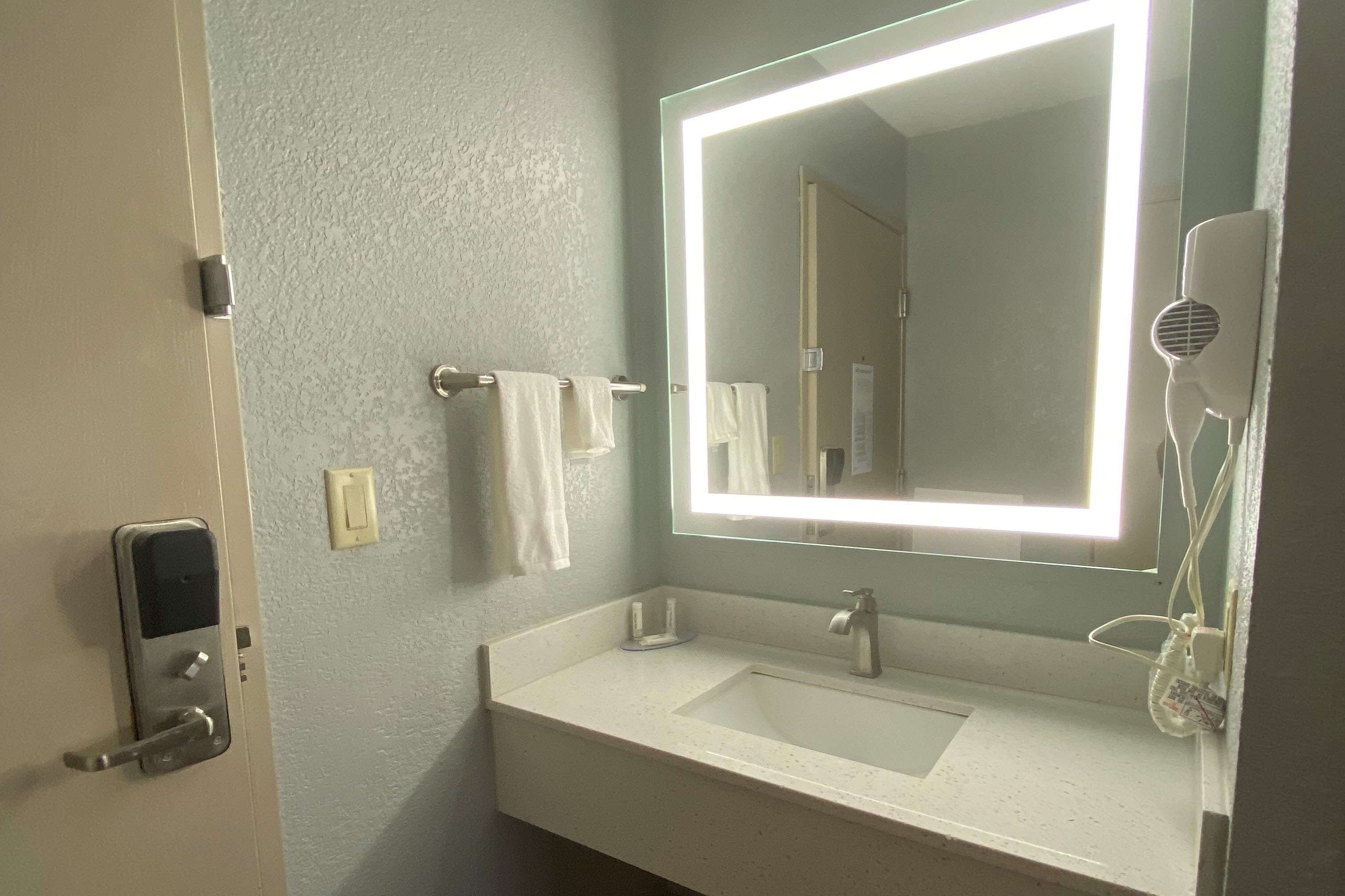A bathroom with a white sink, a mirror with a lighted frame, a towel rack, and a hairdryer.