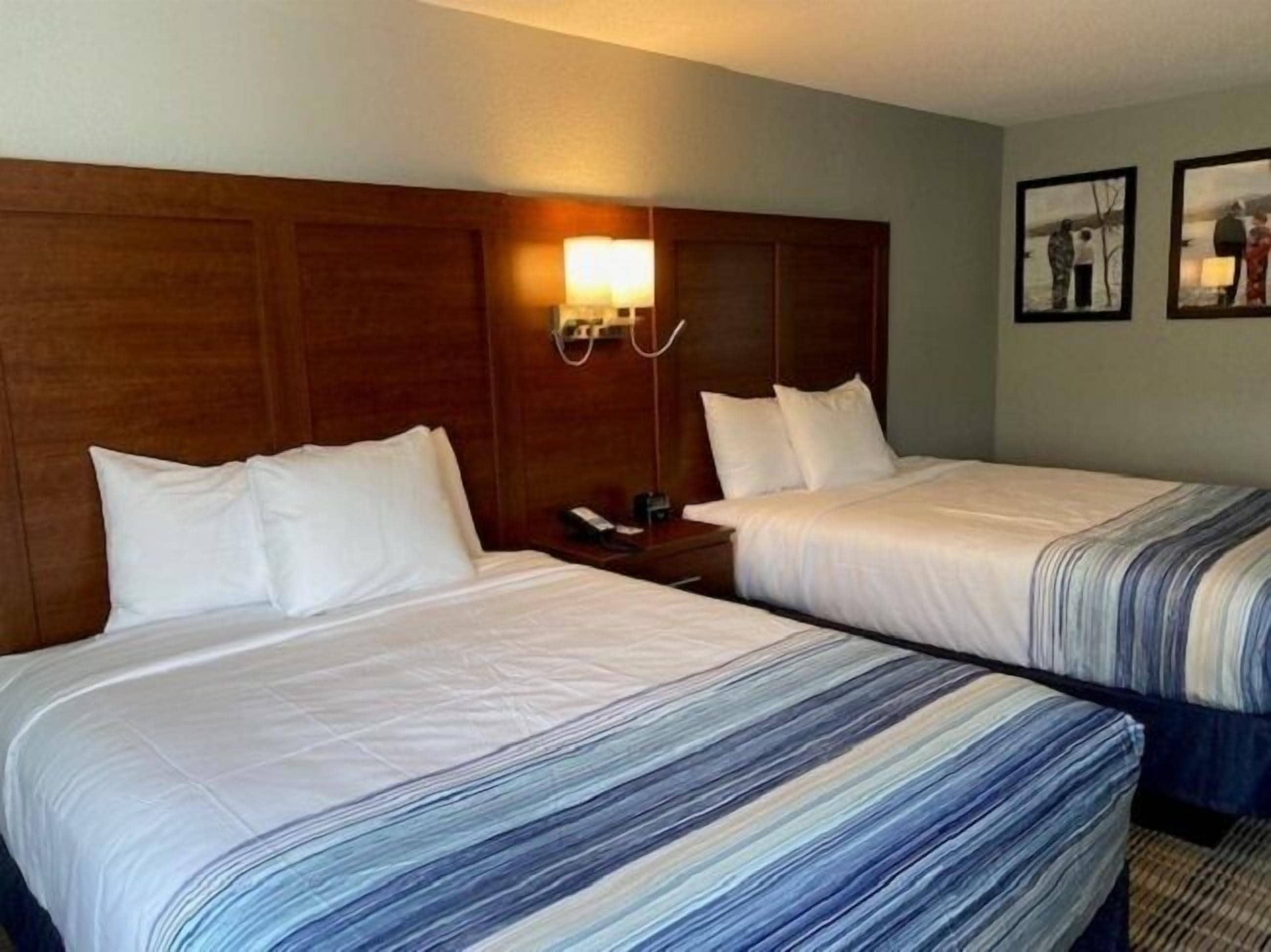 A hotel room with two beds, a wooden headboard, a bedside table with a lamp, and a wall-mounted phone.