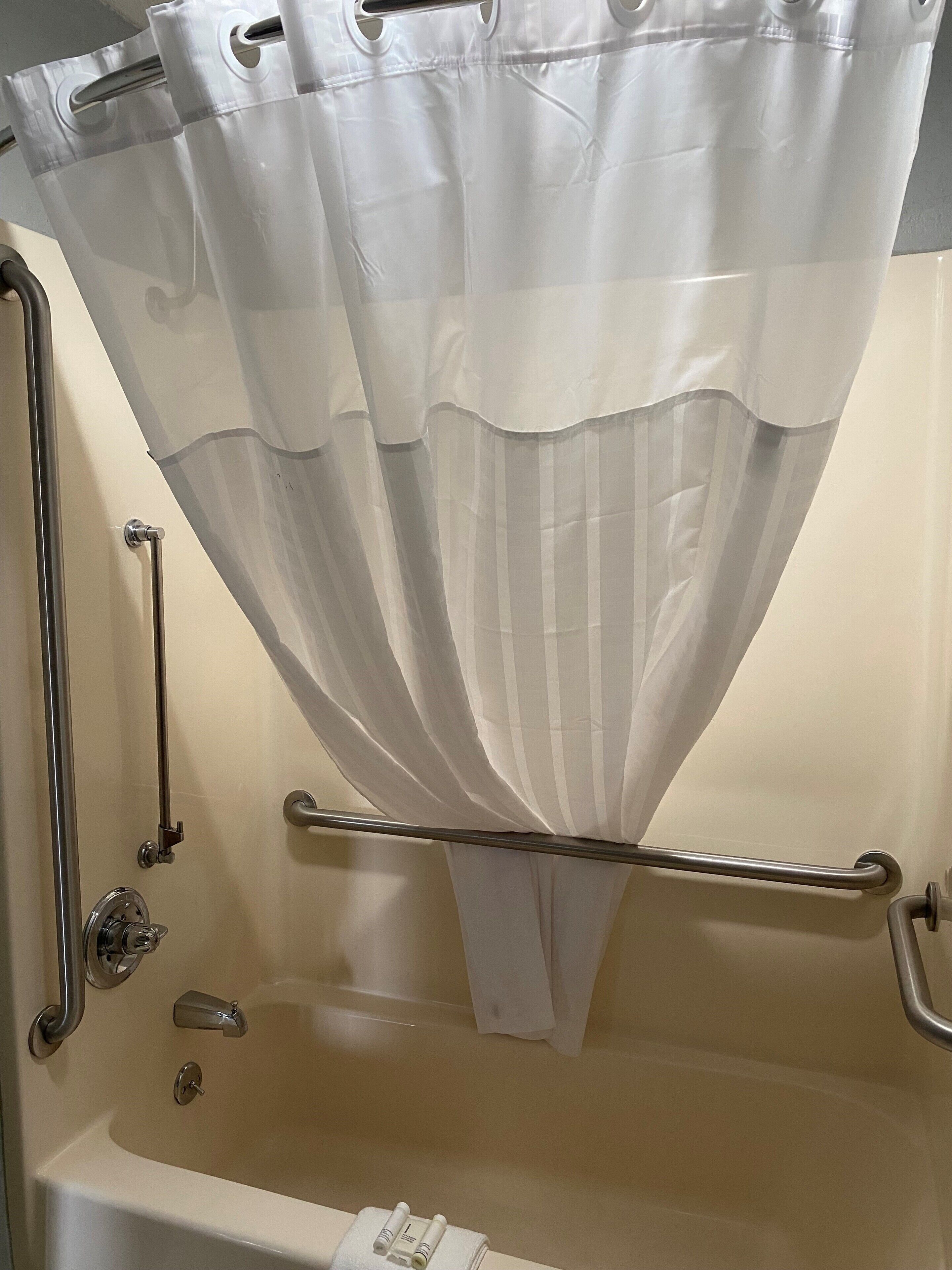 A bathroom with a bathtub, grab bars, and a shower curtain.