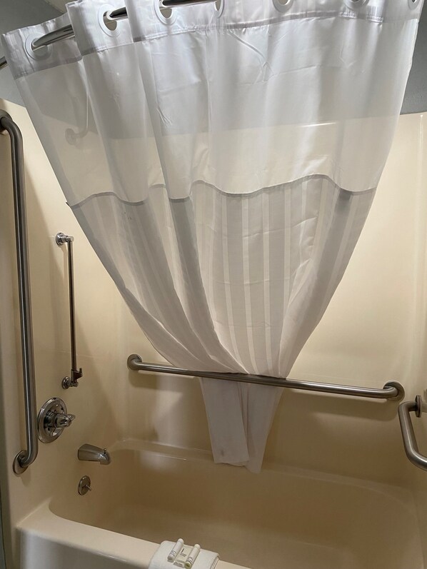 A bathroom with a bathtub, grab bars, and a shower curtain. - AmericInn by Wyndham Williamsburg (South Amana)