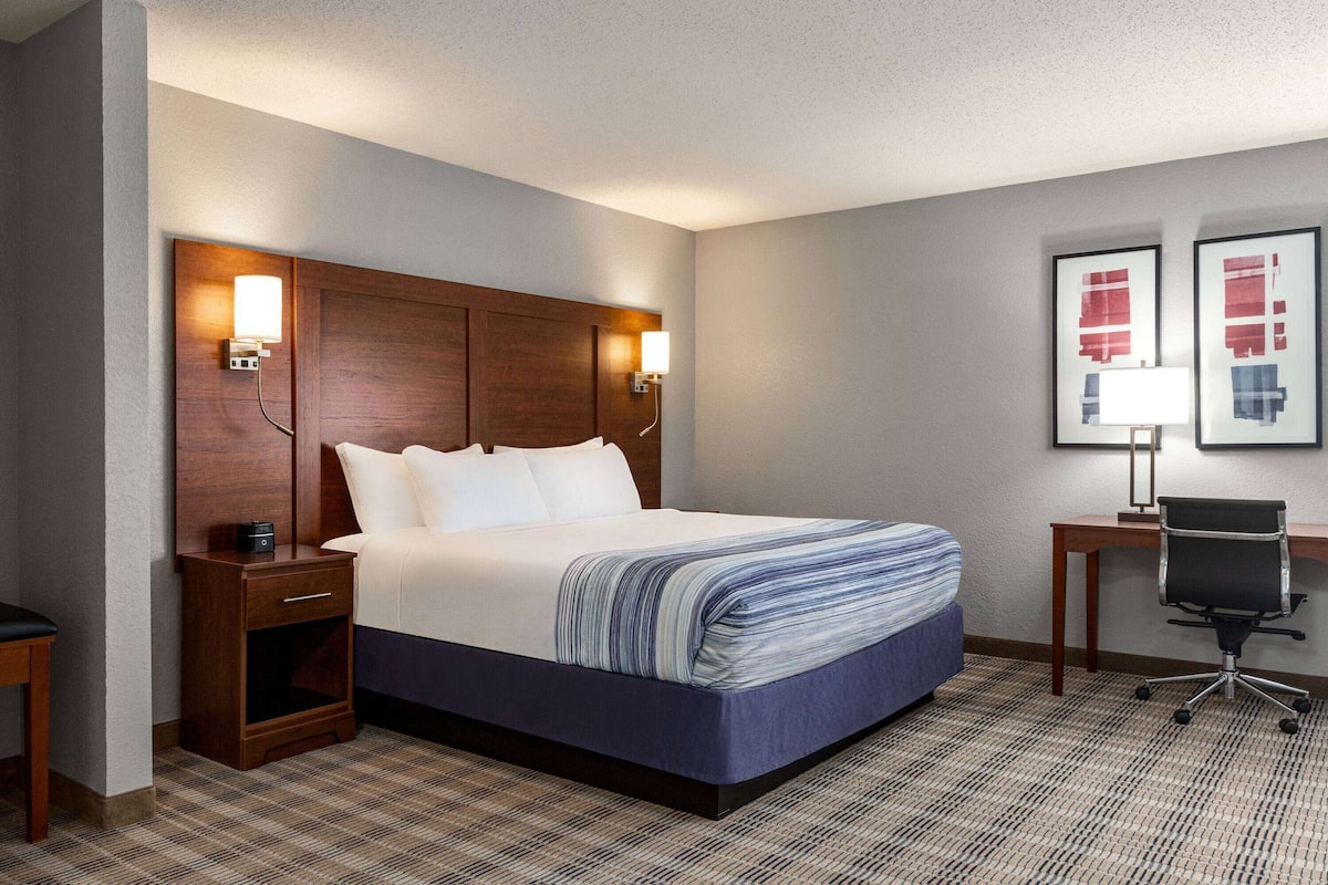 A hotel room with a large bed, wooden headboard, bedside lamps, a desk, and a chair.