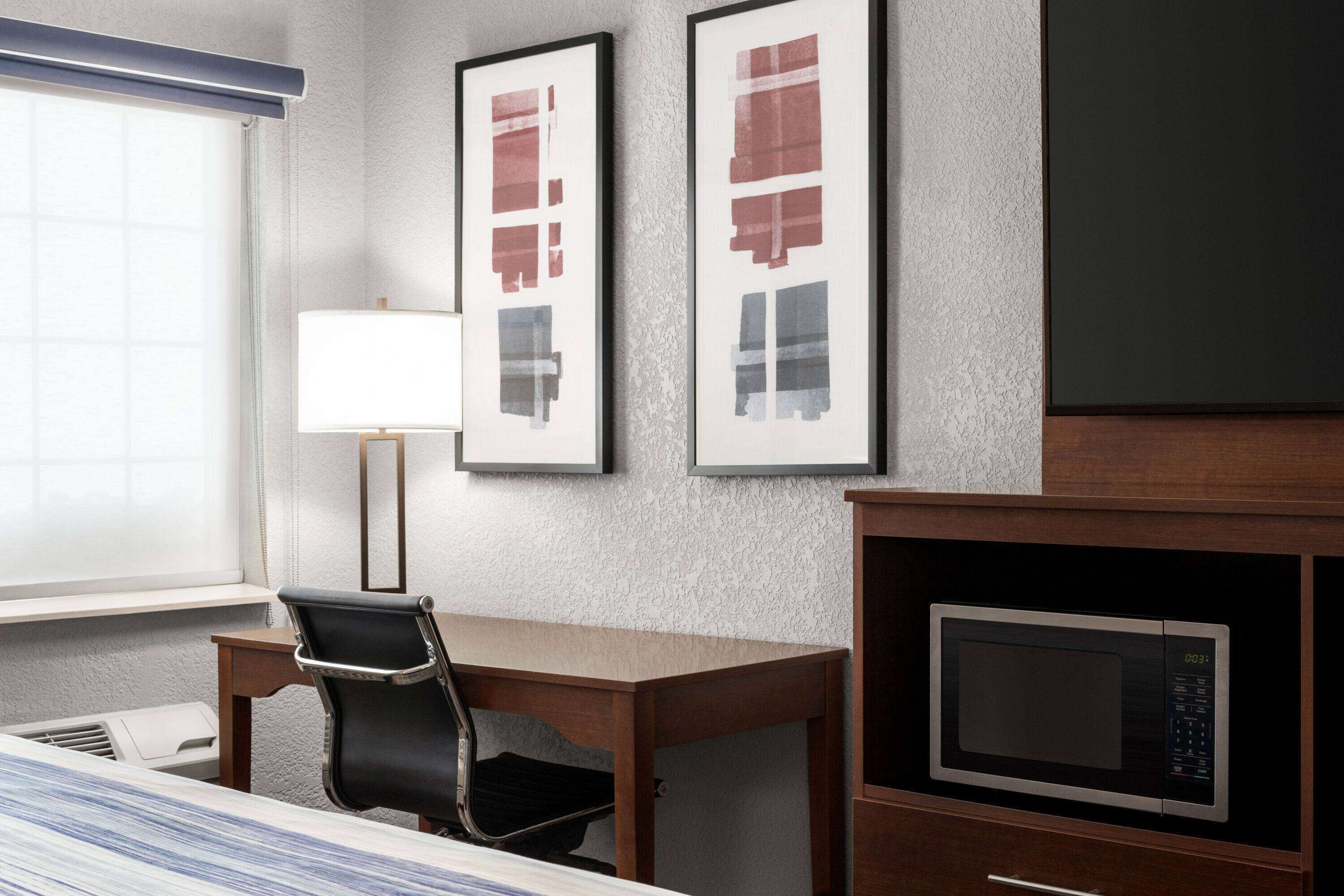 Habitación de hotel con cama, escritorio, silla, lámpara y microondas.