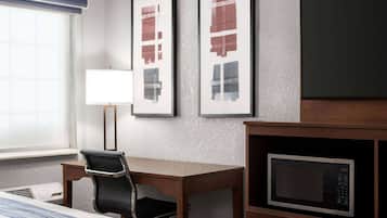 Habitación de hotel con cama, escritorio, silla, lámpara y microondas.