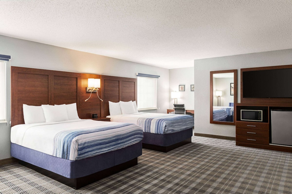A hotel room with two beds, a flat-screen TV, a desk with a lamp, and a large mirror.