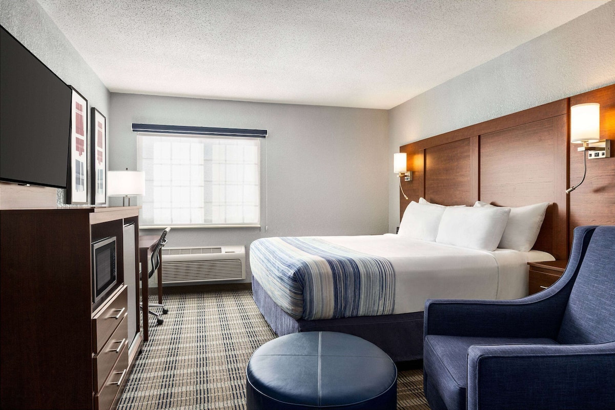 A hotel room with a bed, a desk, a television, a chair, and a window with blinds.