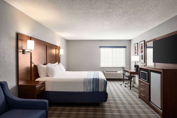 A hotel room with a bed, a desk, a chair, a TV, and a window. - AmericInn by Wyndham Williamsburg (South Amana)