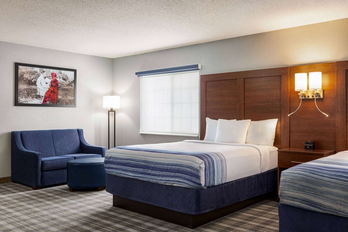 A hotel room with a large bed, a sofa, a small table, and a wall-mounted lamp.