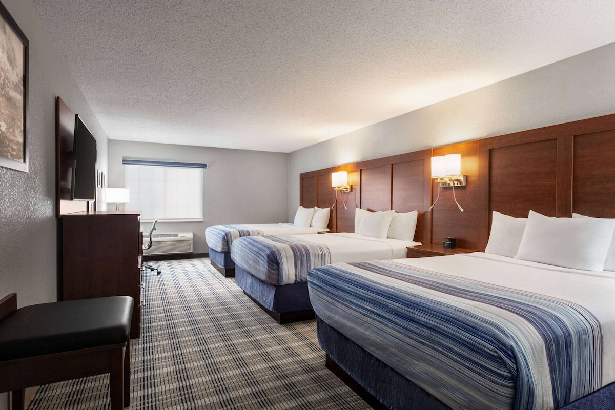 A hotel room with three beds, a desk, a chair, a TV, and a window with blinds.