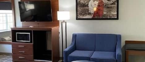 A hotel room with a blue sofa, a television on a wooden cabinet, a framed picture on the wall, and a patterned carpet.