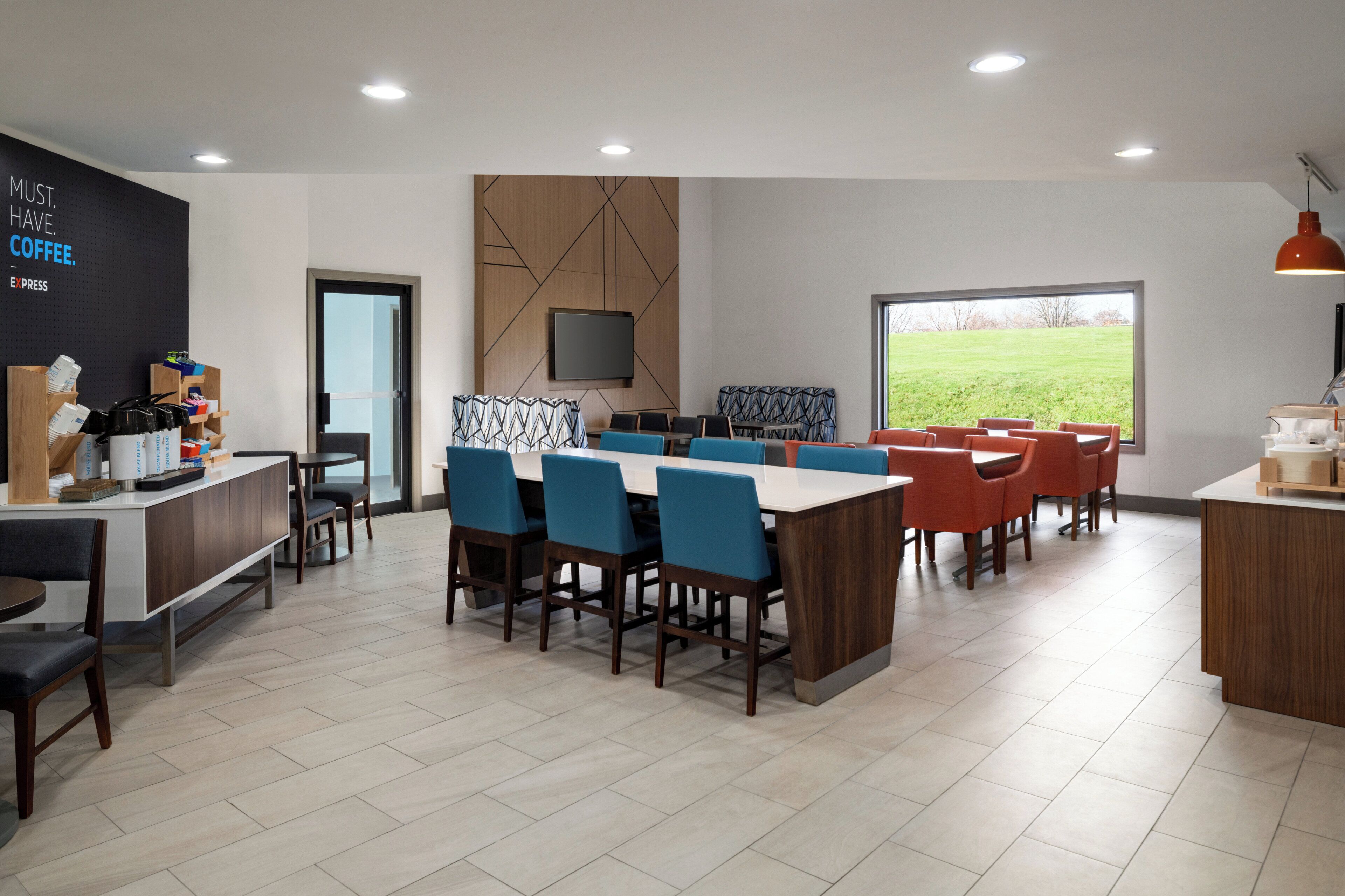 A modern kitchen with a dining area, a coffee station, and a large window offering a view of the outdoors.