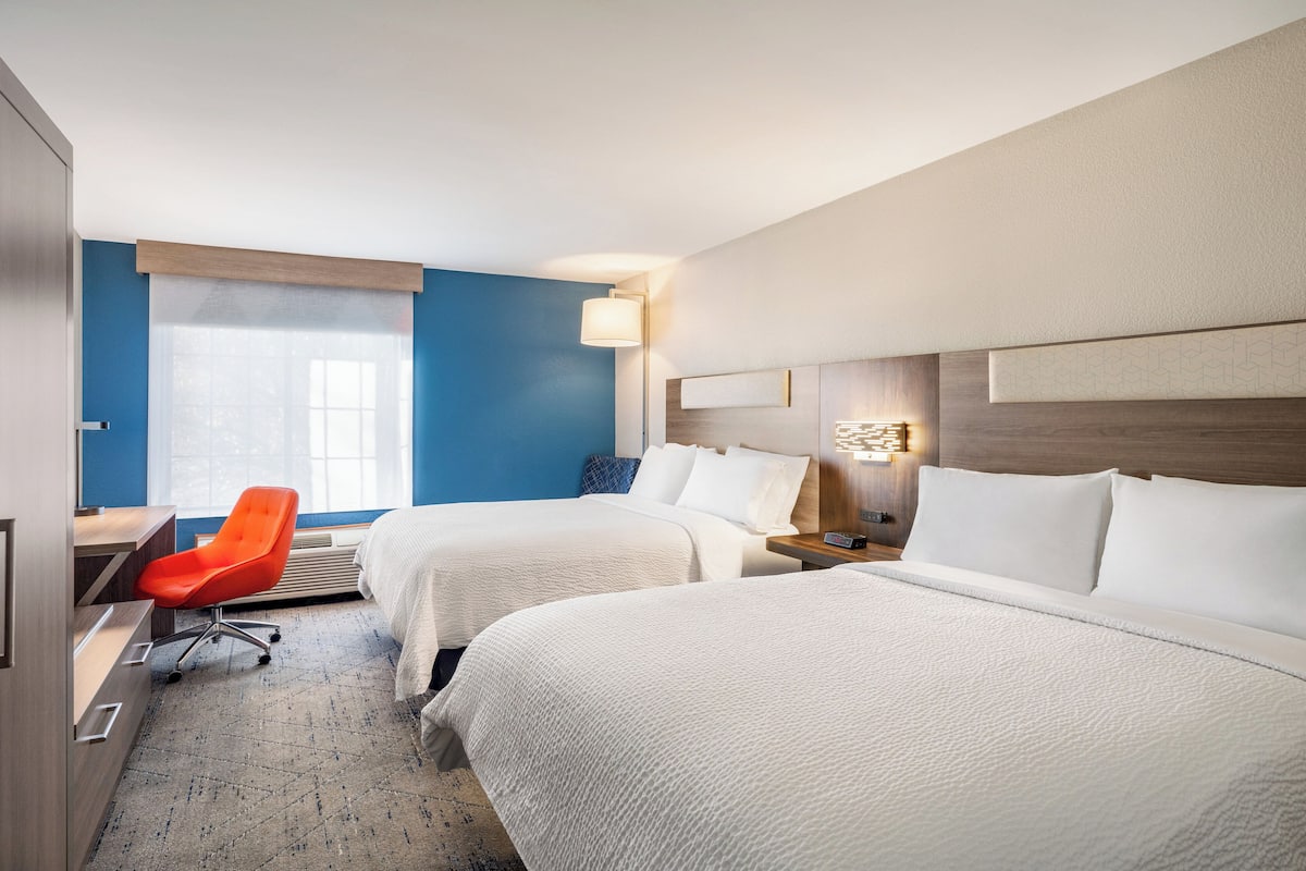 A hotel room with two beds, a desk, a chair, and a window with blinds.