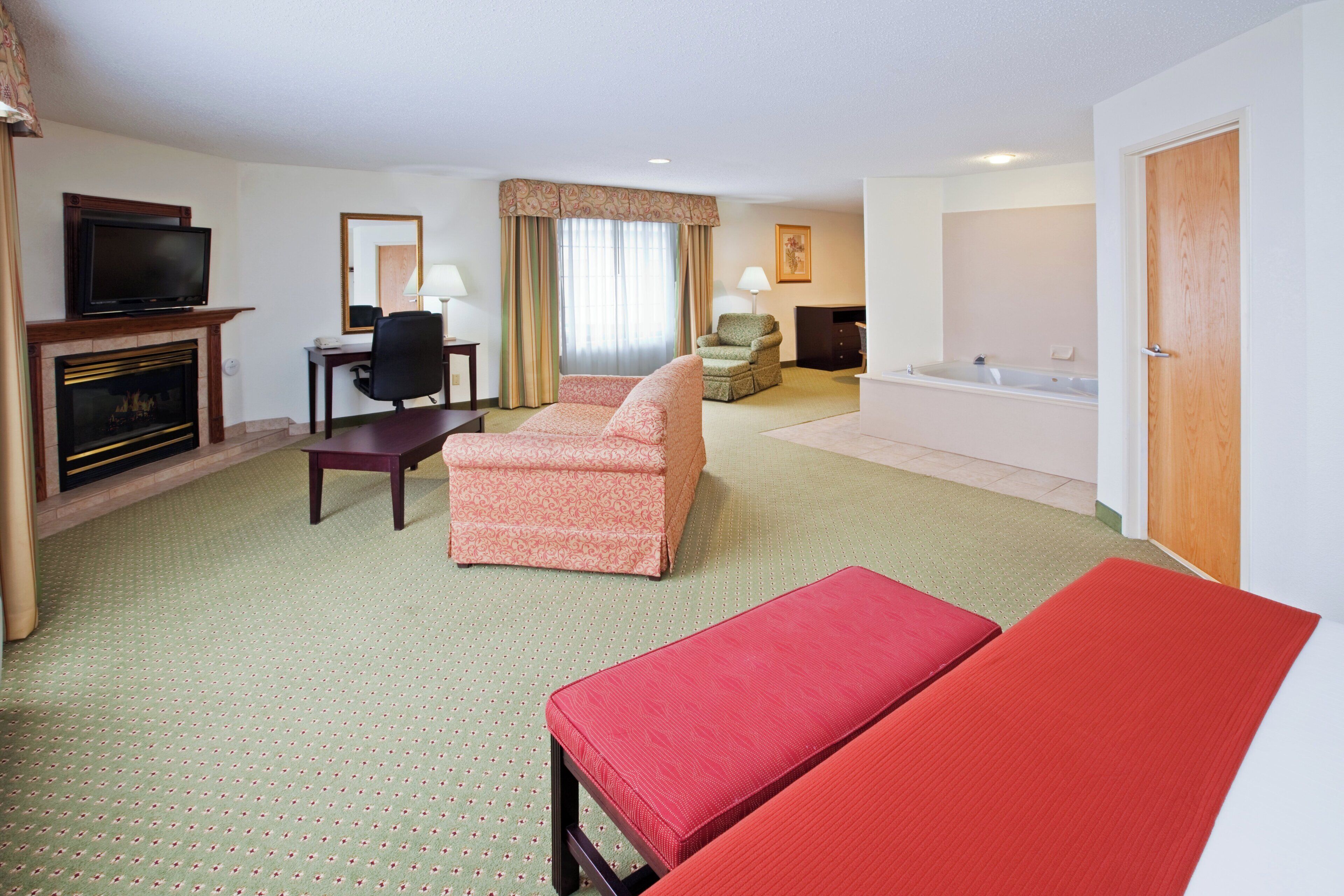 A hotel room with a sofa, a chair, a desk, a television, a fireplace, and a bathtub.