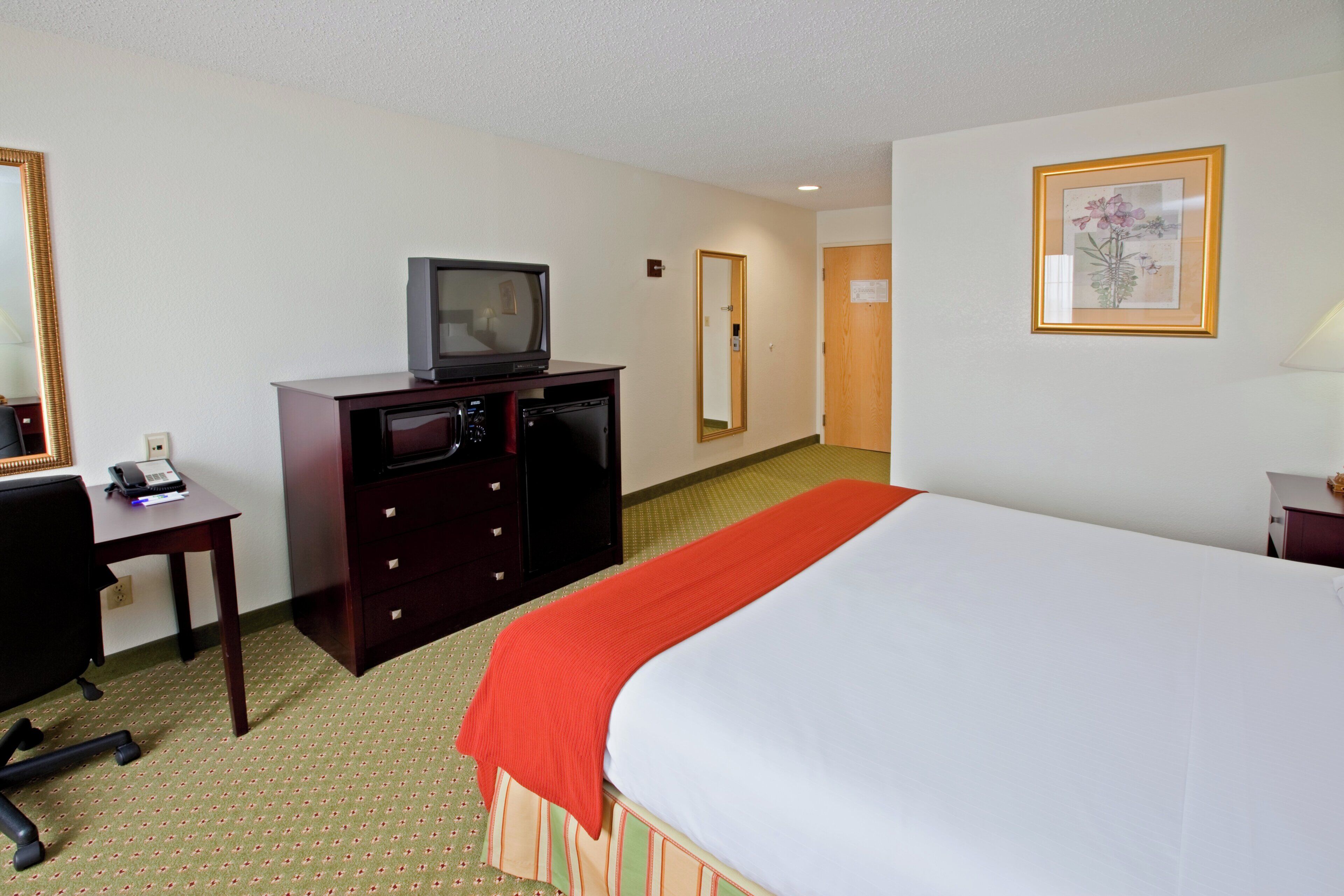 Una habitación de hotel con una cama, un escritorio con teléfono, televisión y espejo.