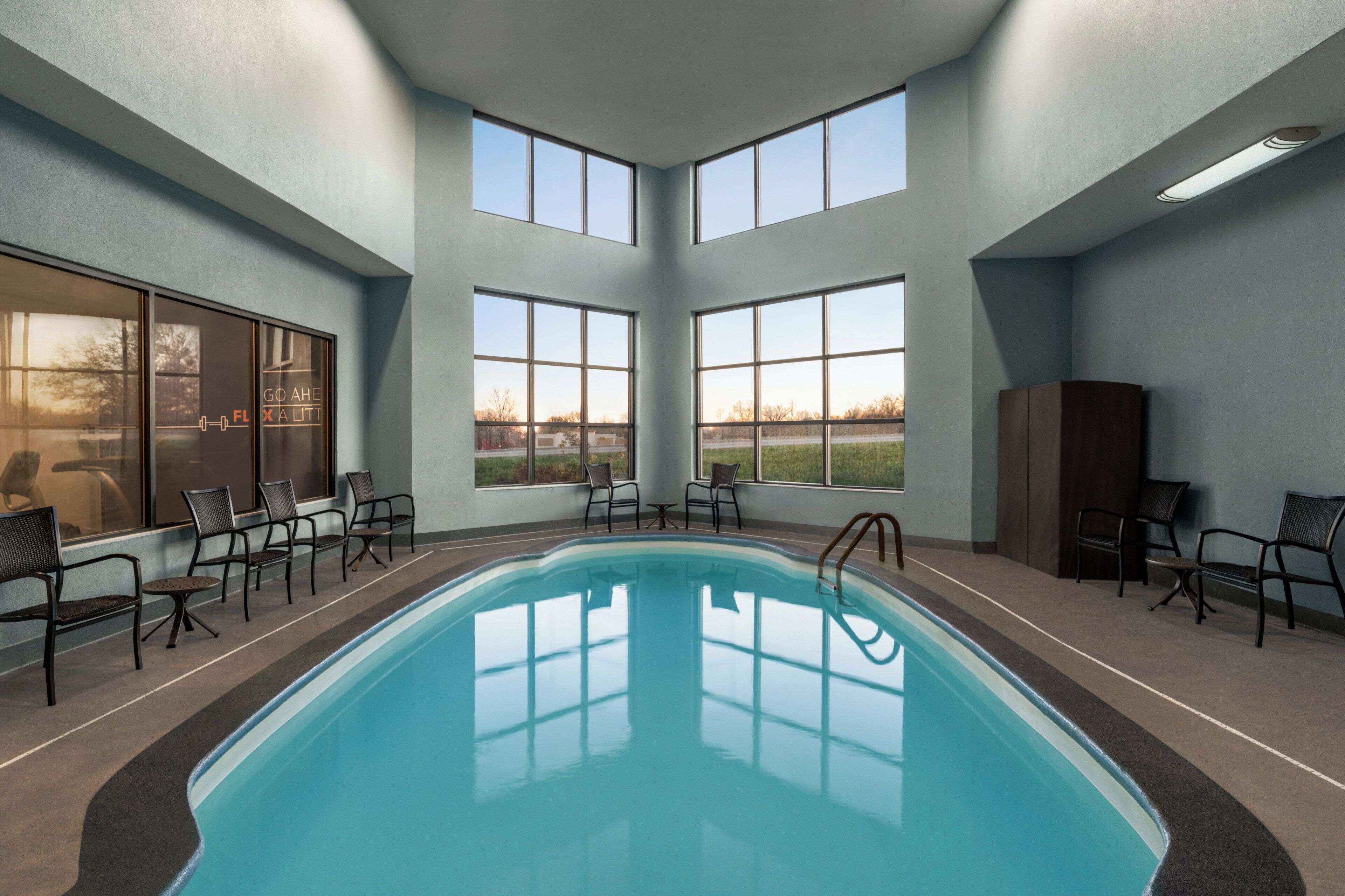 Una piscina interior con ventanas transparentes, sillas y vistas al exterior.