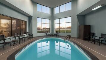 Una piscina interior con ventanas transparentes, sillas y vistas al exterior.