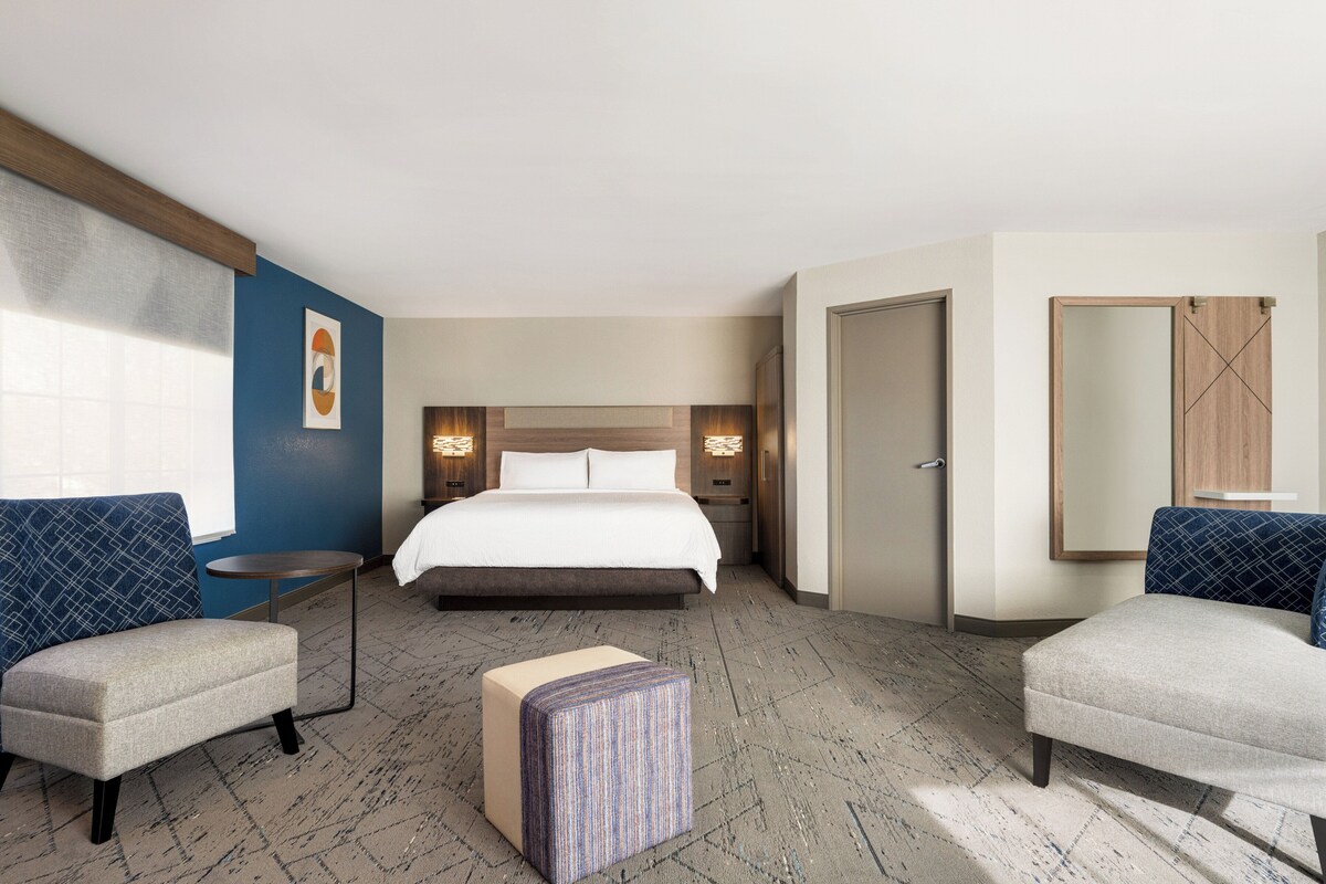 Ein Hotelzimmer mit einem Bett, zwei Sesseln, einem kleinen Tisch, einem Spiegel und einer Tür.
