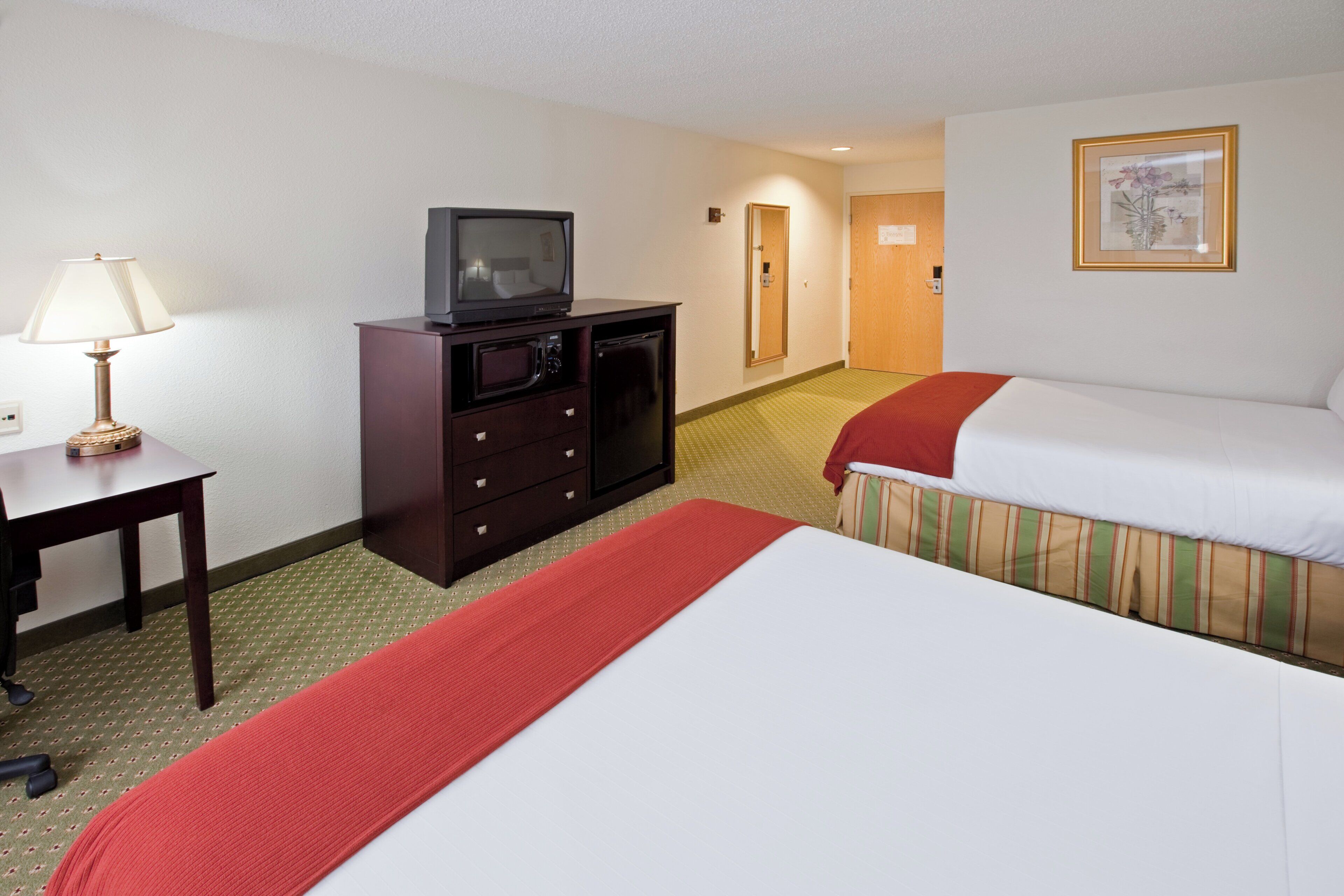 Una habitación de hotel con una cama, un escritorio con lámpara, un televisor, un microondas y un aparador.