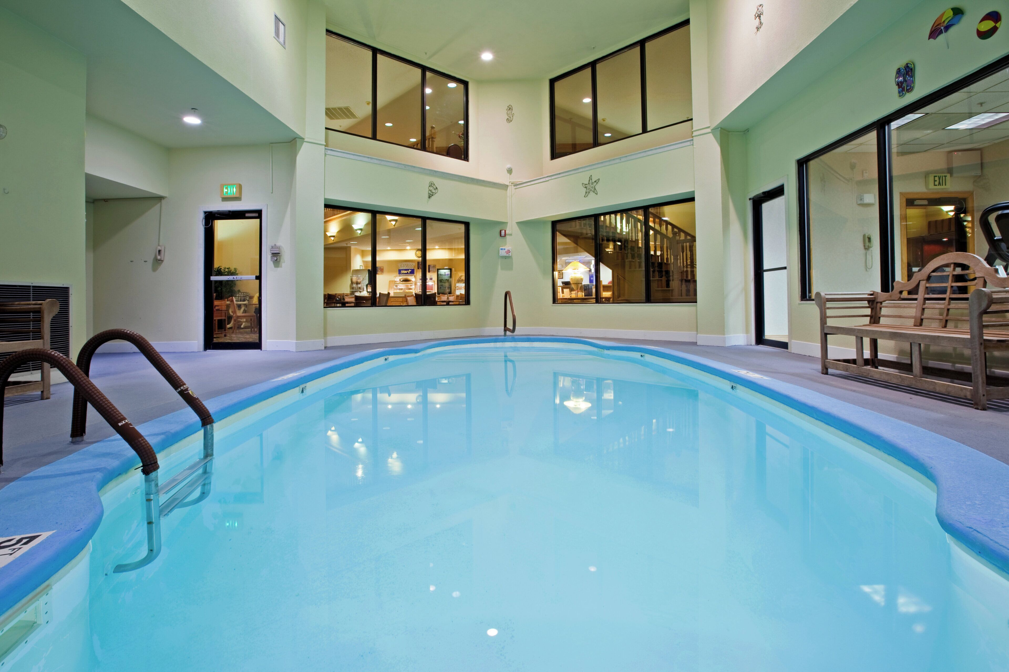 A swimming pool with clear water, surrounded by a lounge area with seating and a view of the interior space.