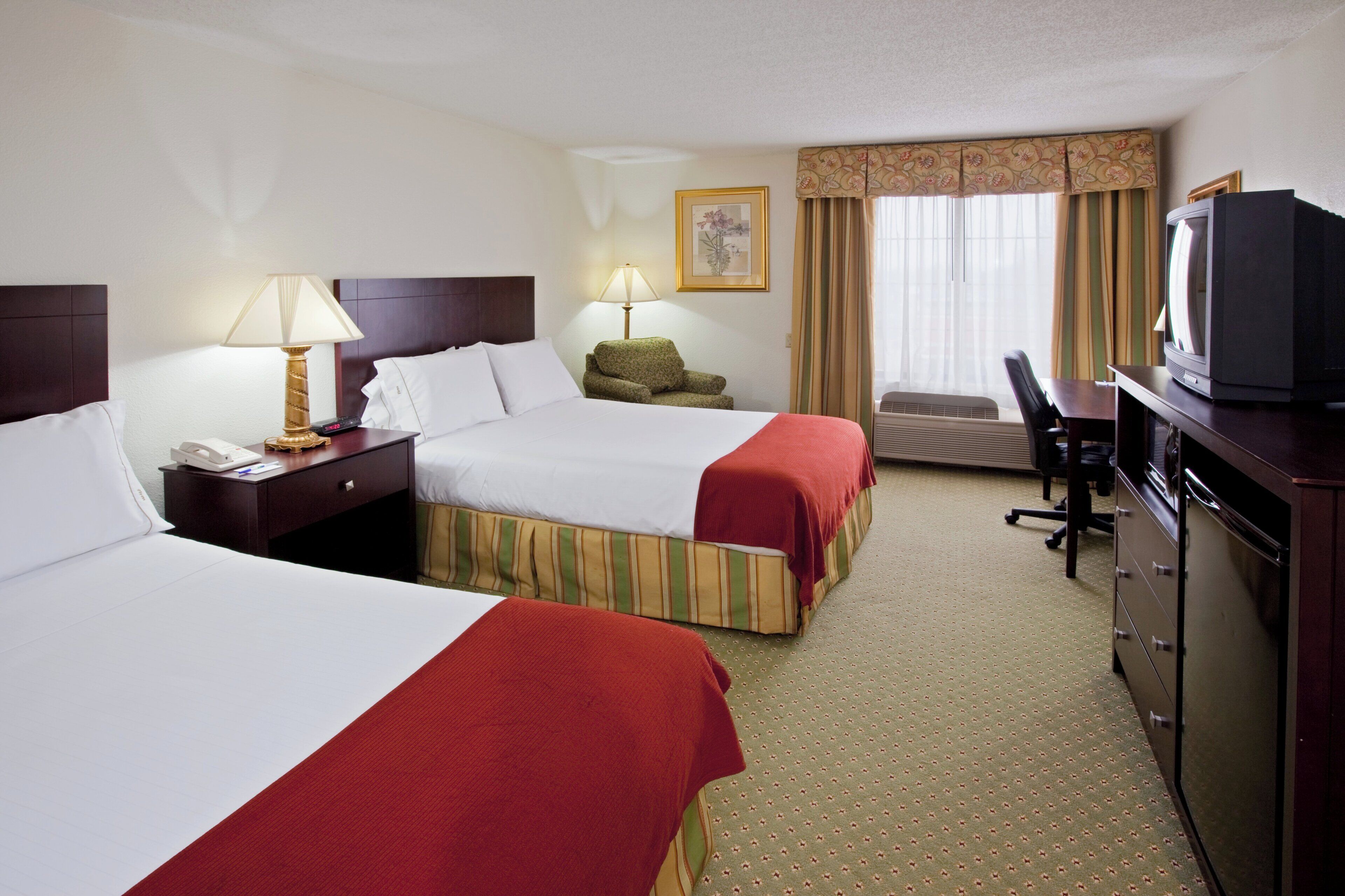 A hotel room with two beds, a desk, a television, and a chair.