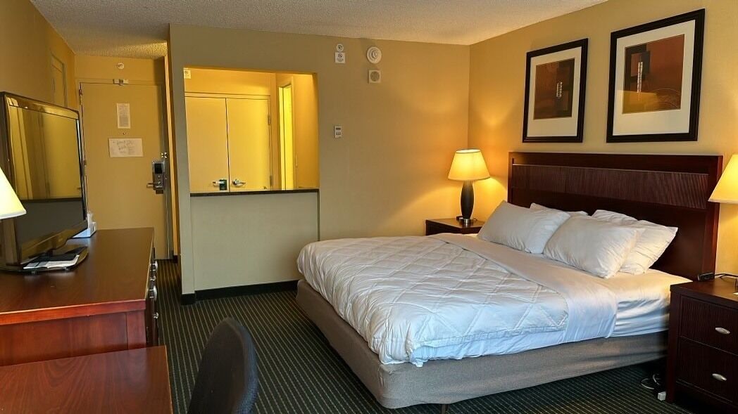 A hotel room with a bed, bedside tables, a desk, a chair, a mirror, and framed pictures on the wall.