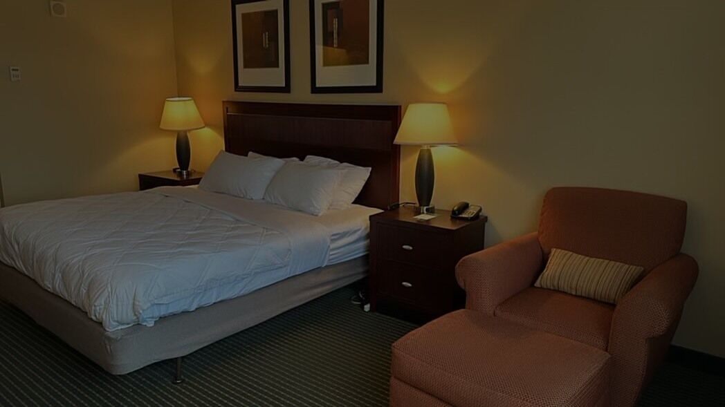 A hotel room with a bed, two bedside tables with lamps, a chair, and a headboard.