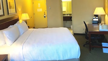 A hotel room with a large bed, two bedside lamps, a desk with a chair, and a small table with a lamp.
