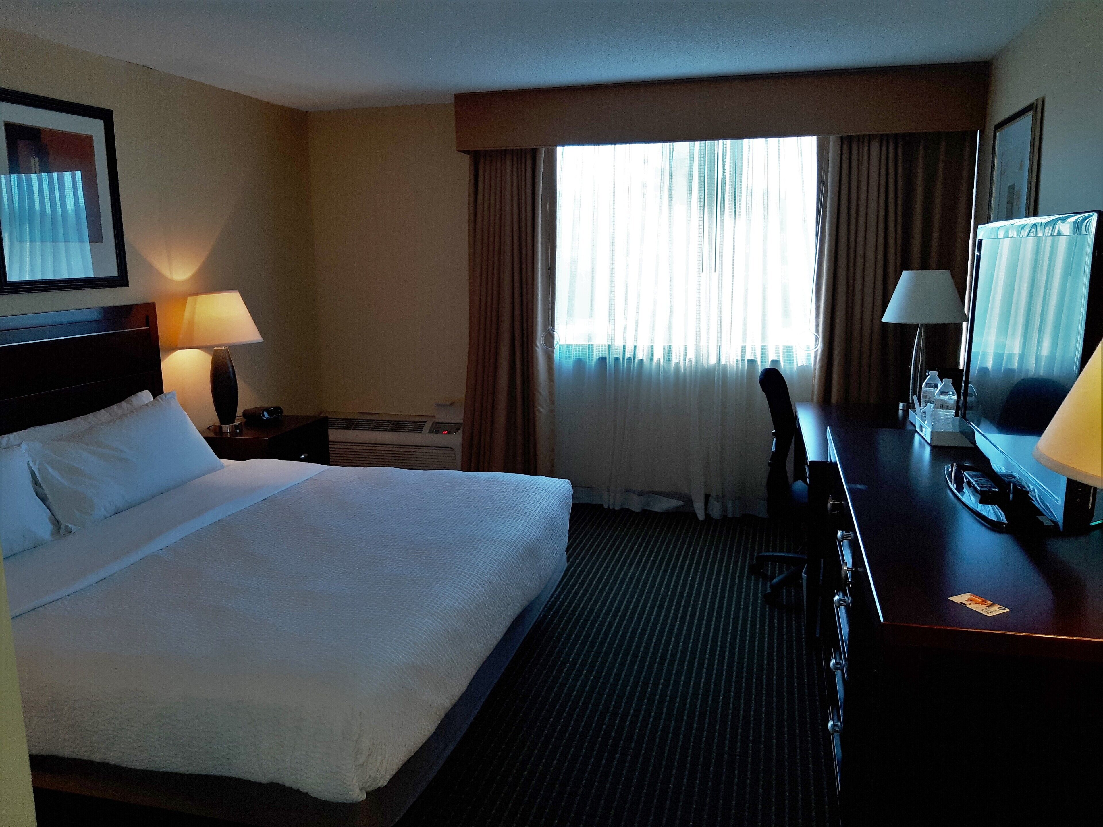 A hotel room with a large bed, a desk with a chair, a TV, and a window with curtains.