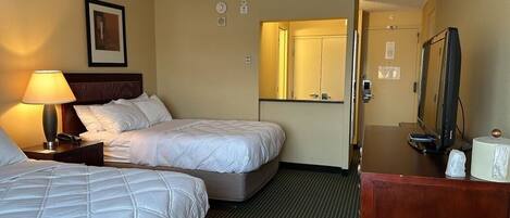 A hotel room with two beds, a desk with a television, a mirror, and a lamp.